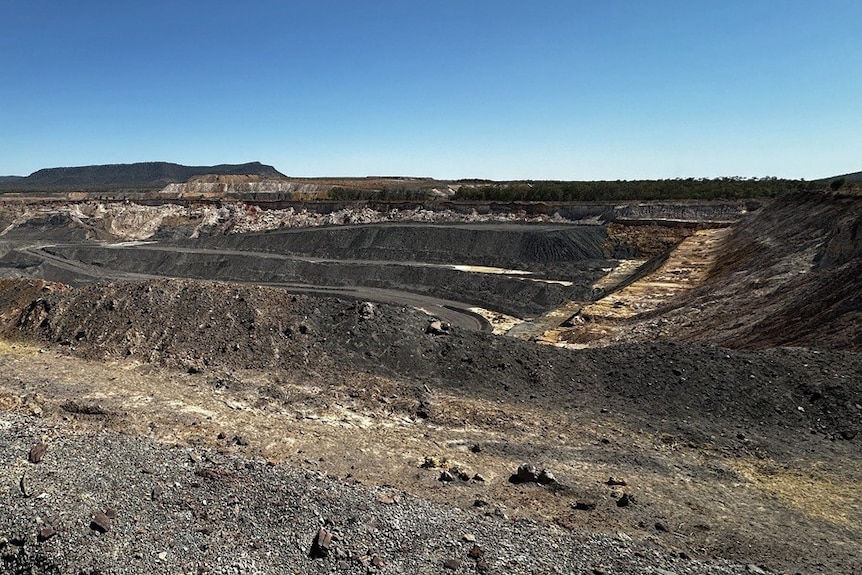 Wide shot of an abandoned mine on a sunny day, surrounded by rocks and gravel