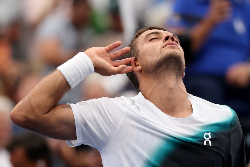 Male tennis player holds hand to ear, encouraging loud cheering