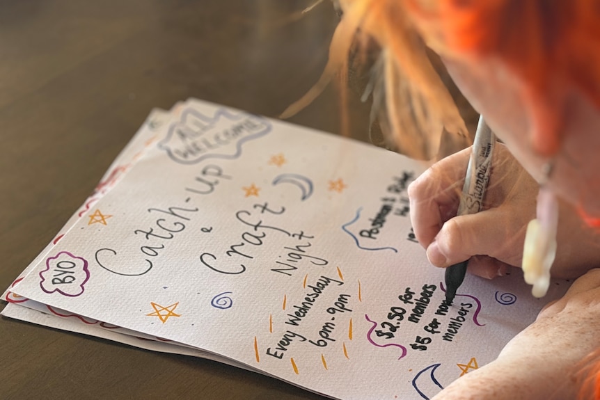 A young woman draws a poster by hand with a coloured pen.