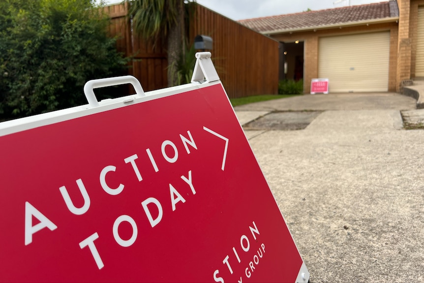 An A-frame sign that reads "auction today", directing toward a house.