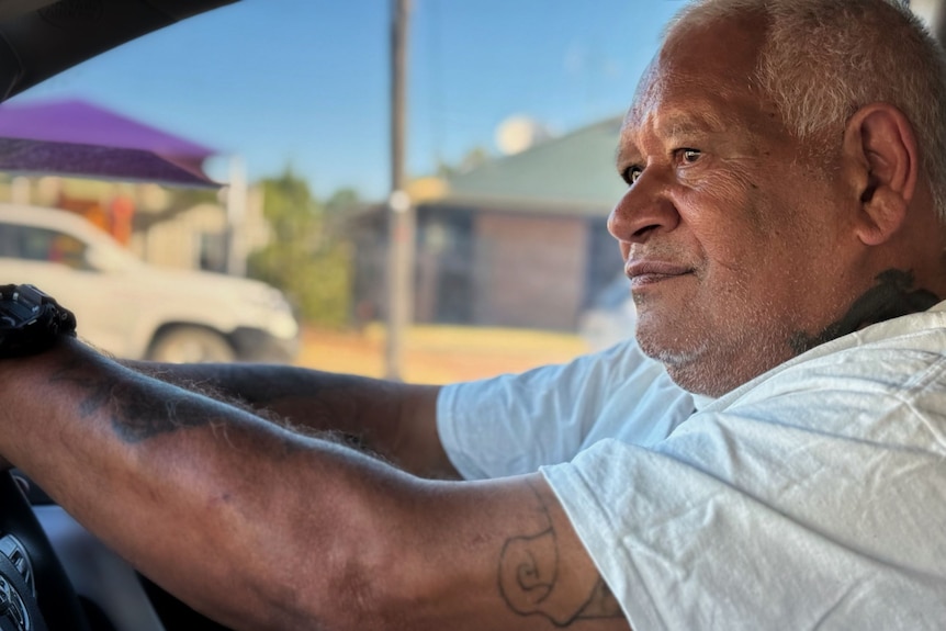 An older Indigenous man sits behind the steering wheel of a car.