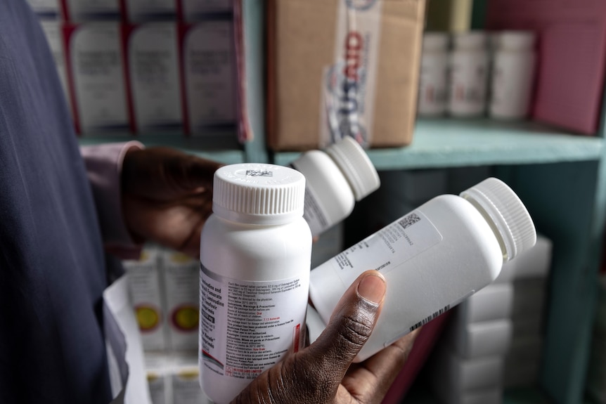 A healthcare worker holds three bottles of HIV antiretroviral tablets.