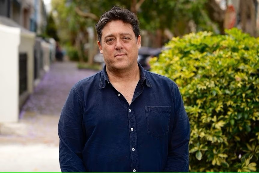 a man in a blue shirt posing in front of green plants