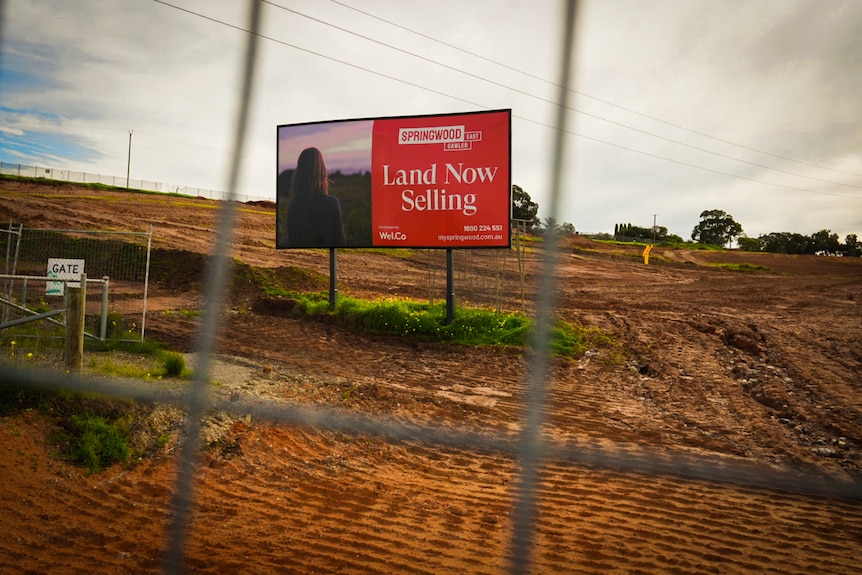 image of a large billboard saying 'land now selling' surrounded by cleared land awaiting housing construction