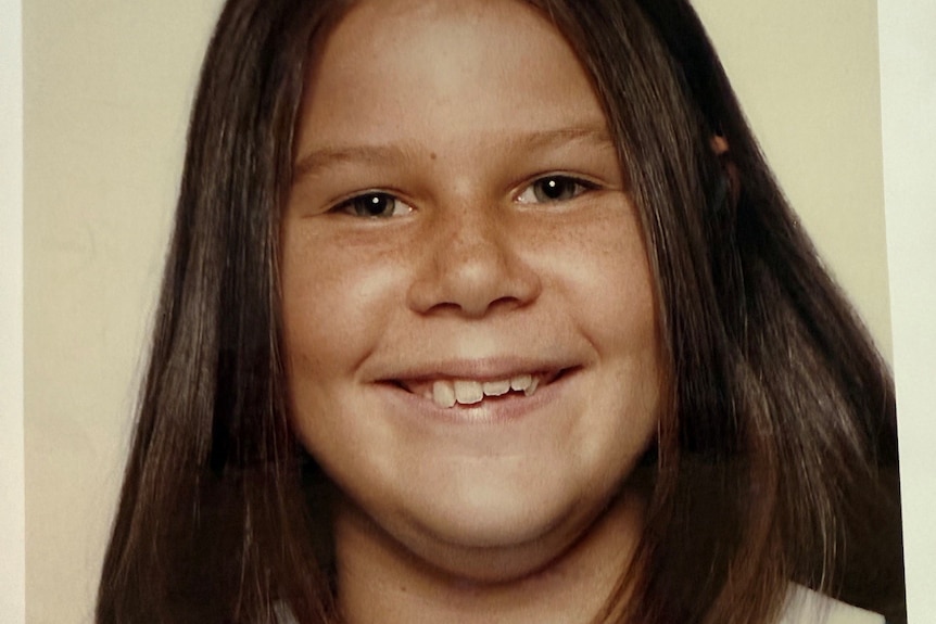 Julia Morris smiles for a portrait in primary school, her brown hair down, wearing a blue and white dress.