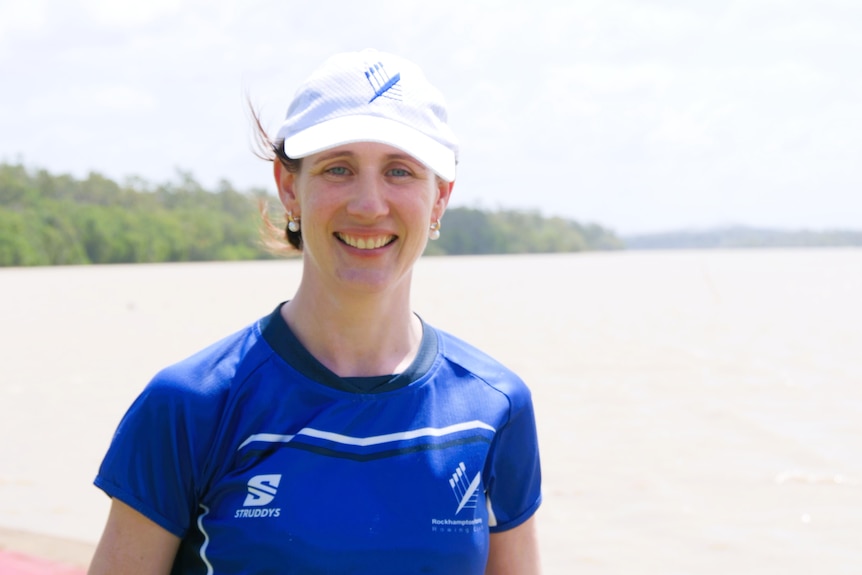 A woman wearing a white cap and blue shirt standing at a river.