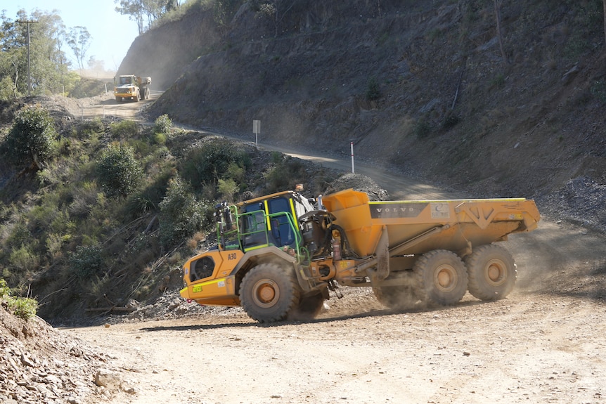Two mine trucks roll down a winding hill towards a mine site 