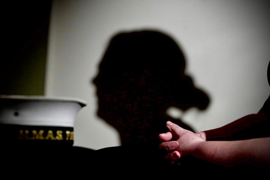 Silhouette against a white wall with navy hat and hands folded in foreground.