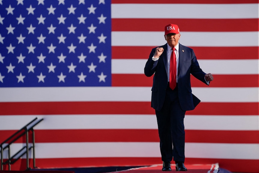 Donald Trump dances in front of a large American flag display.