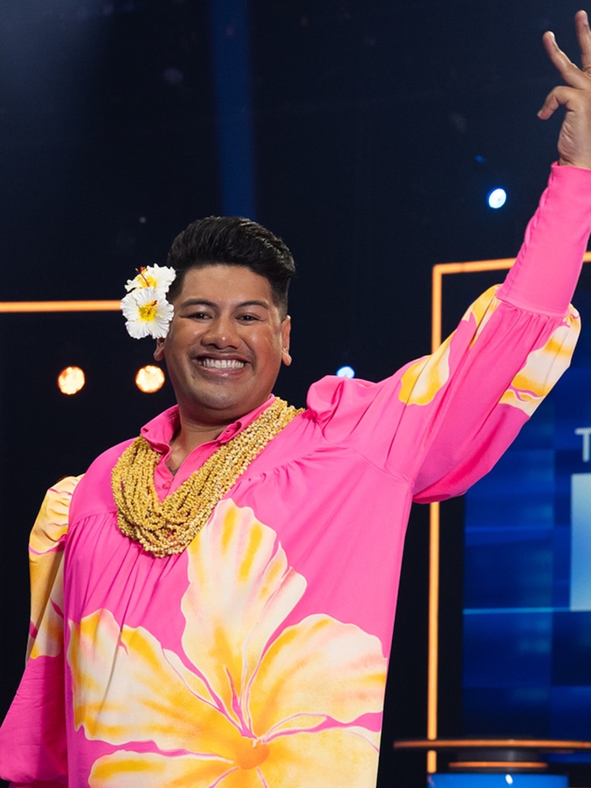 A man in a pink shirt and a flower in his ear waving.