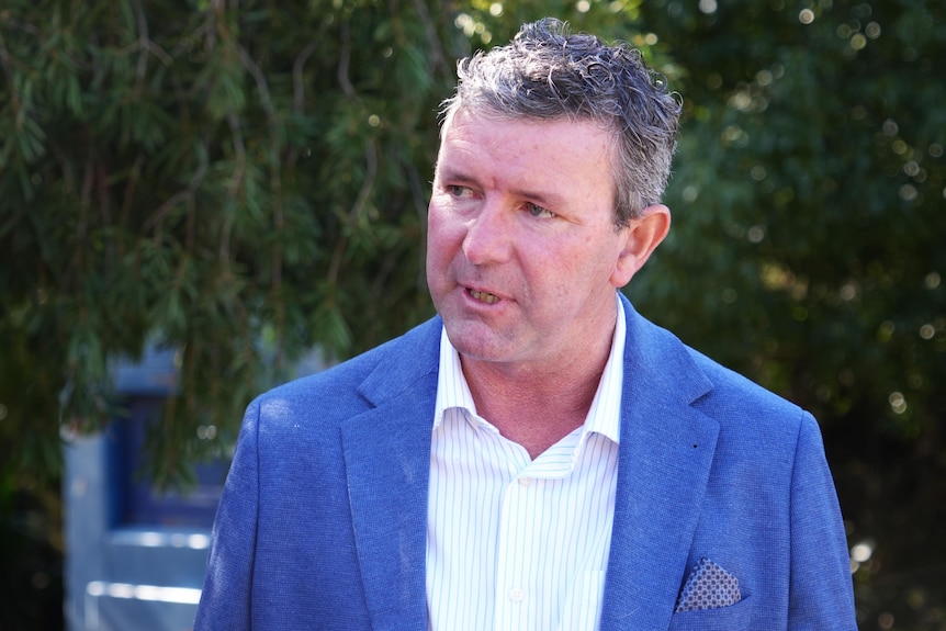 A man in a blue suit talks to someone out of view