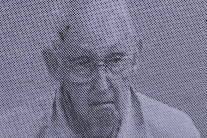 a grainy black and white photo shows an elderly man with glasses and a serious expression