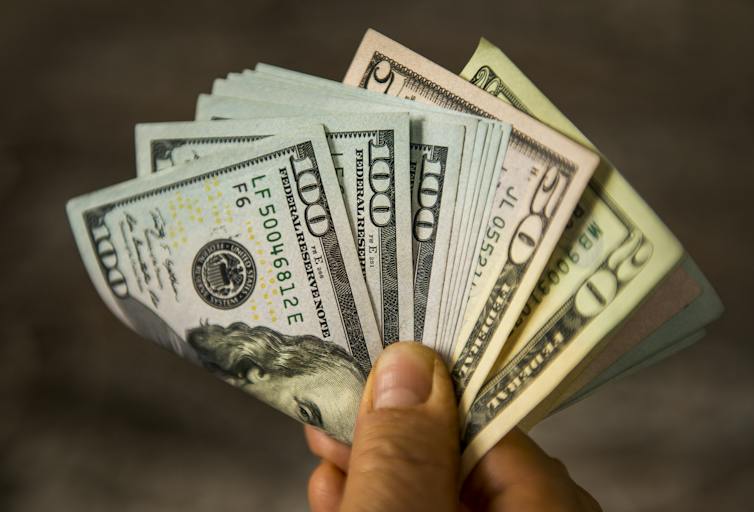 A person holds a big pile of U.S. cash between their fingers, including several $100 bills.