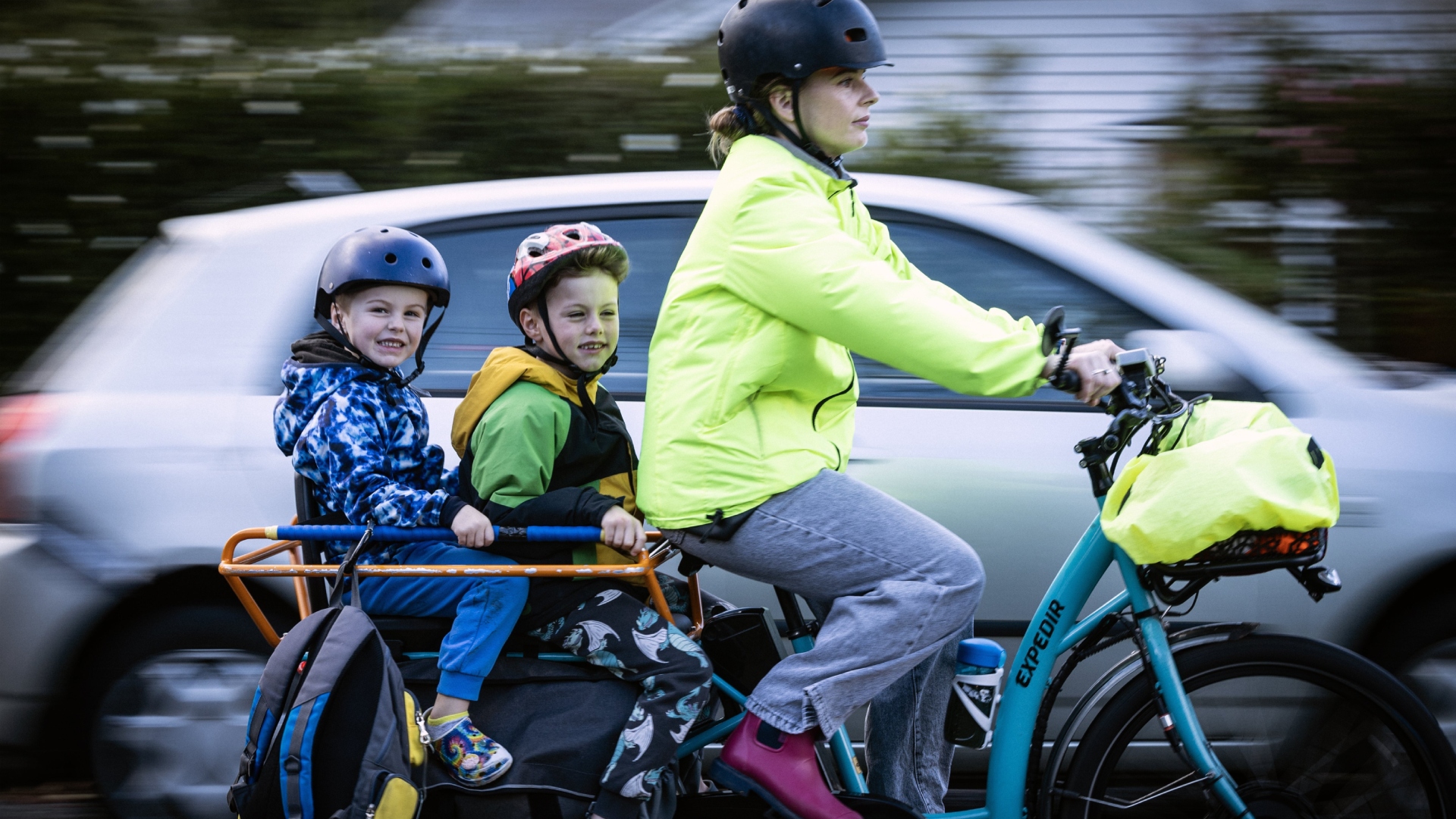 A woman pedals a cargo ebike with 2 children on the back