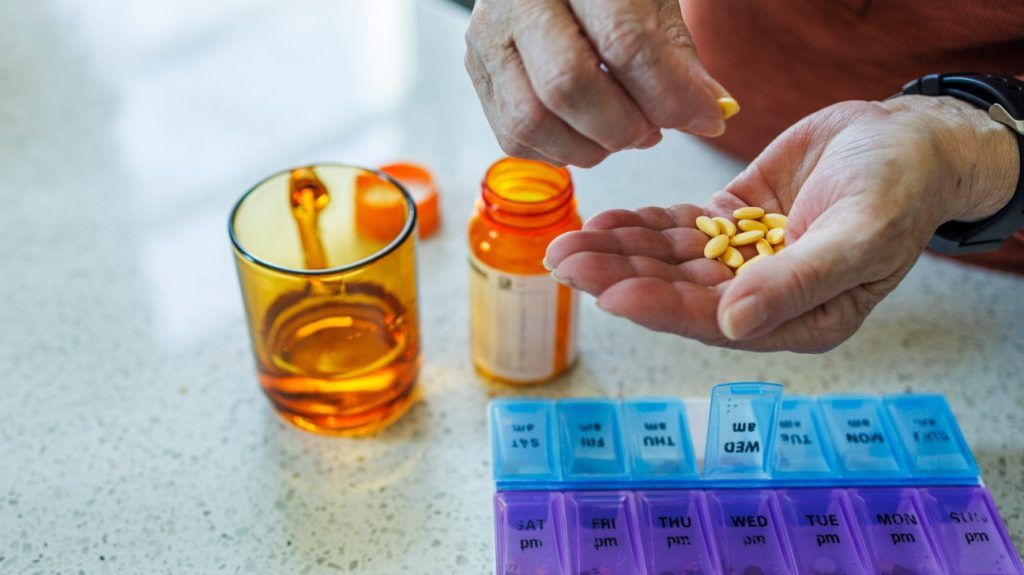An older adults organizing their pills into a weekly dose organizer.
