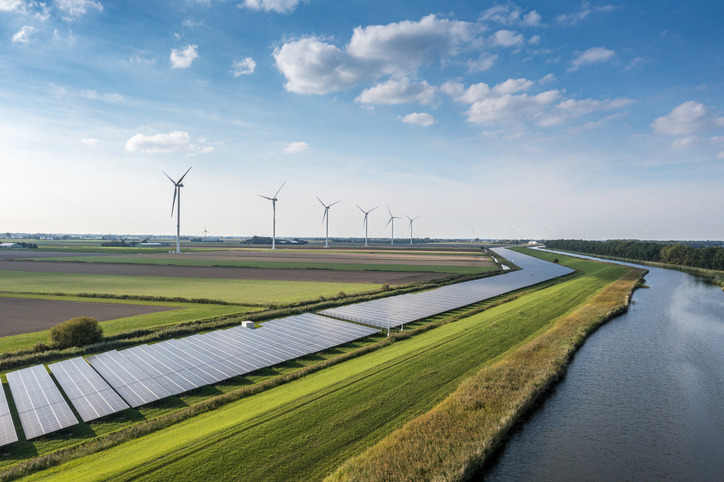 Solar panels and wind turbines in a lush green field in the country.