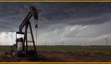 A close up of an oil rig with wind turbines in the background.