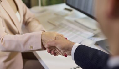A closeup of two businesspeople shaking hands while sitting in front of a computer.