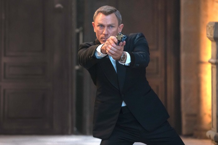 Daniel Craig as James Bond in No Time to Die Daniel Craig as James Bond, wearing a smart suit and pointing a gun.