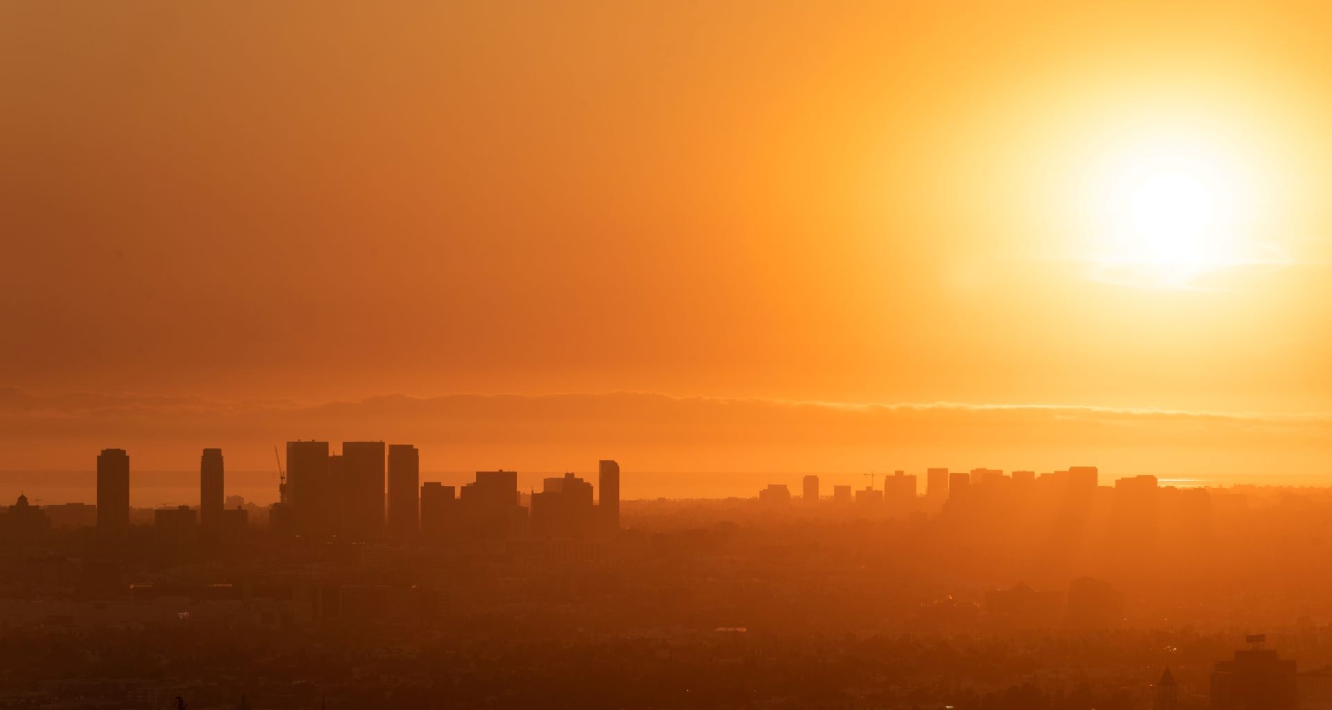 A city skyline silhouetted against a bright orange sunset.