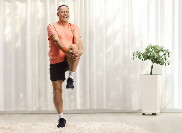 Mature man in sportswear stretching his leg and smiling at home