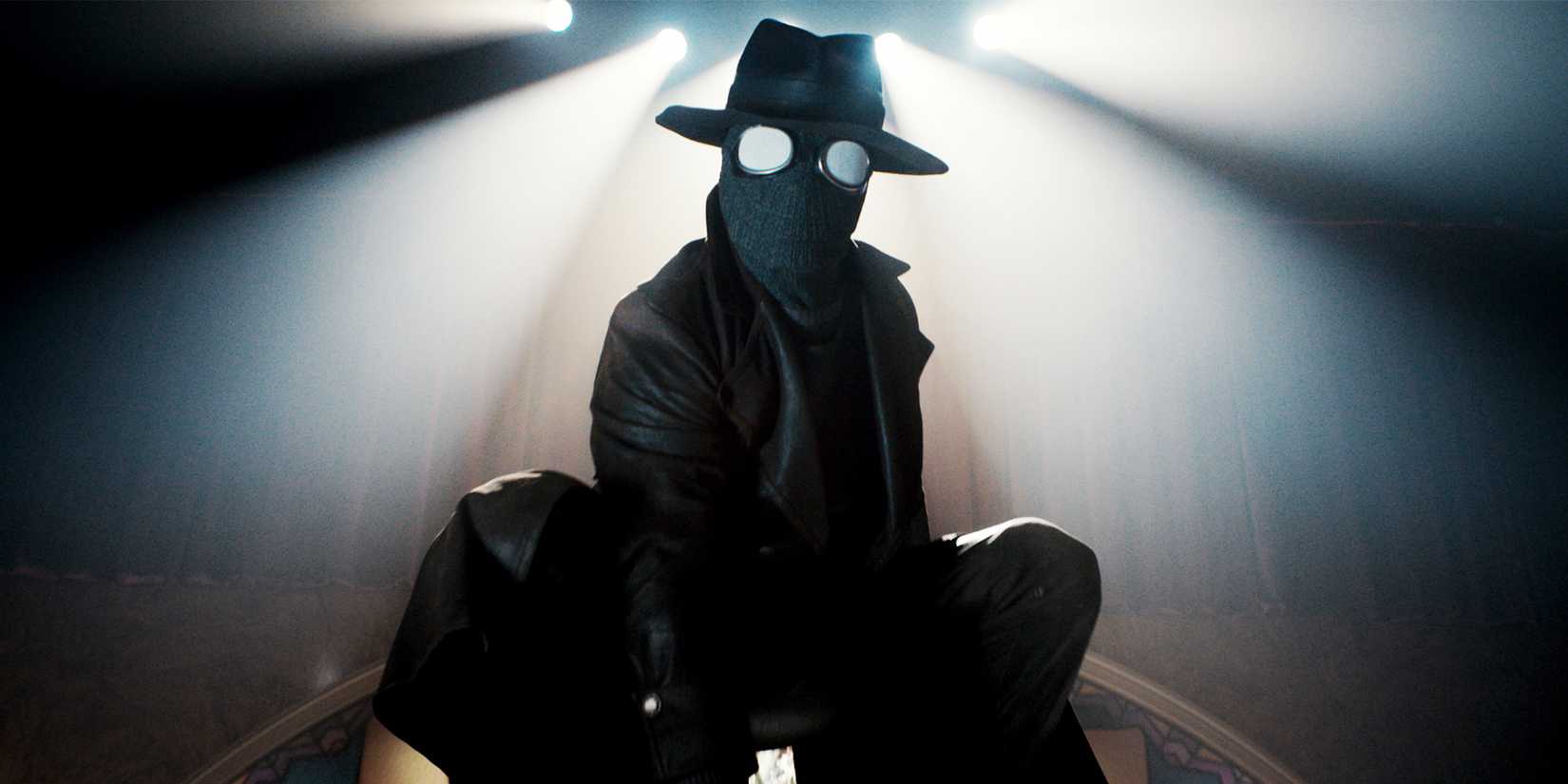 Nicolas Cage as The Spider crouched on a desk in costume in Spider-Noir
