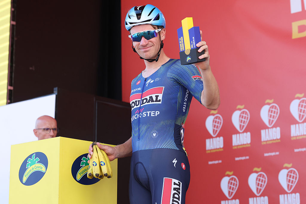 Ethan Hayter on the sign on podium of stage 12 of the 2026 Vuelta holding a small trophy and a bunch of bananas