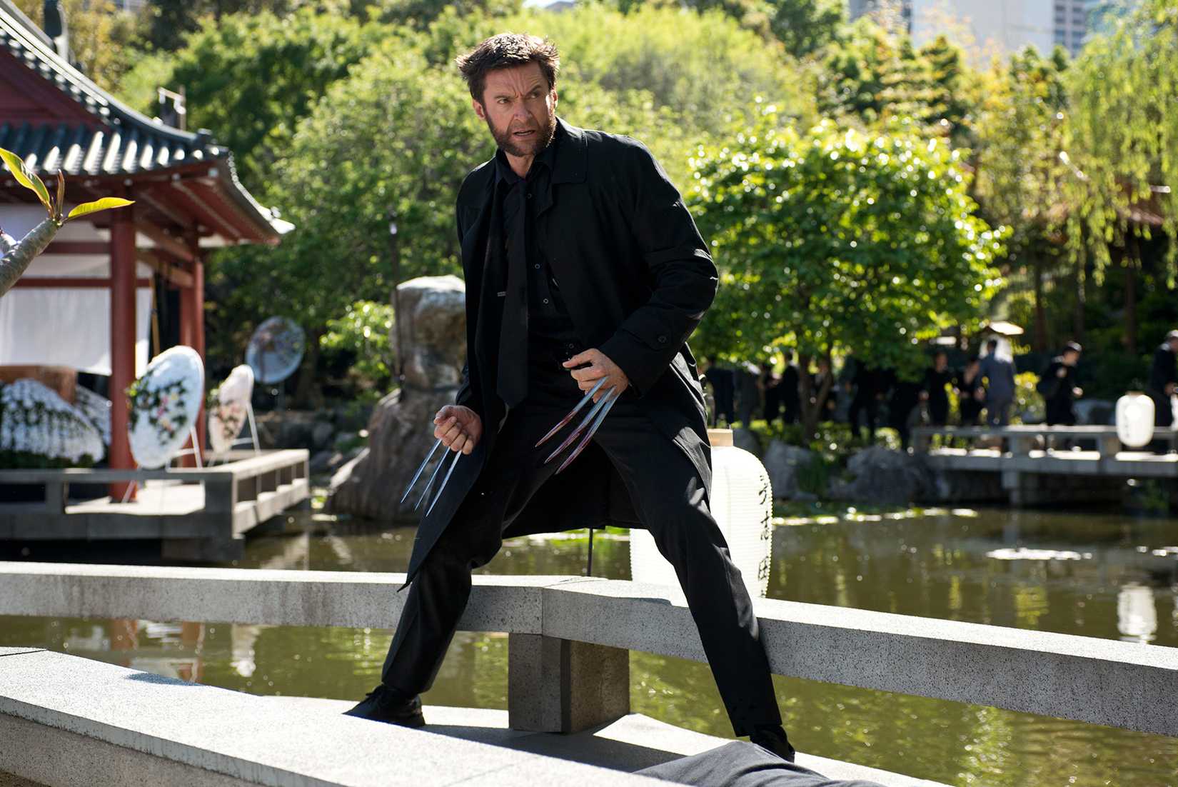Wolverine, played by Hugh Jackman, stands on a ledge near a river. His pose is defensive — he has his claws extended and is standing ready for a fight. He is, however, wearing a nice jacket.