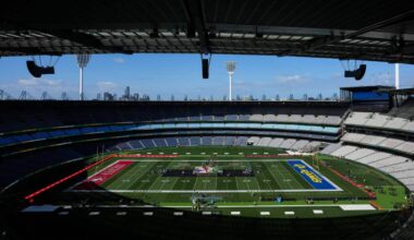 Wide view of a large stadium configured for an American football event, with team-branded end zones, a stage at midfield and mostly empty seating.