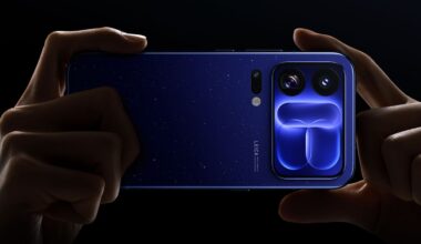A pair of hands holds a dark blue smartphone with a starry pattern on the back and a prominent camera module featuring two large lenses and a distinct, glowing blue geometric design.