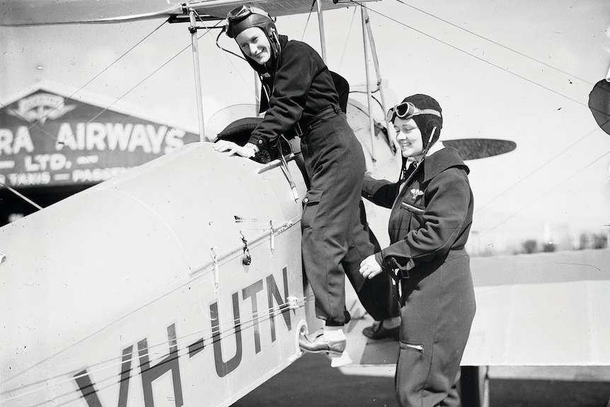 Black and white image of two women at the cockpit of a biplane.