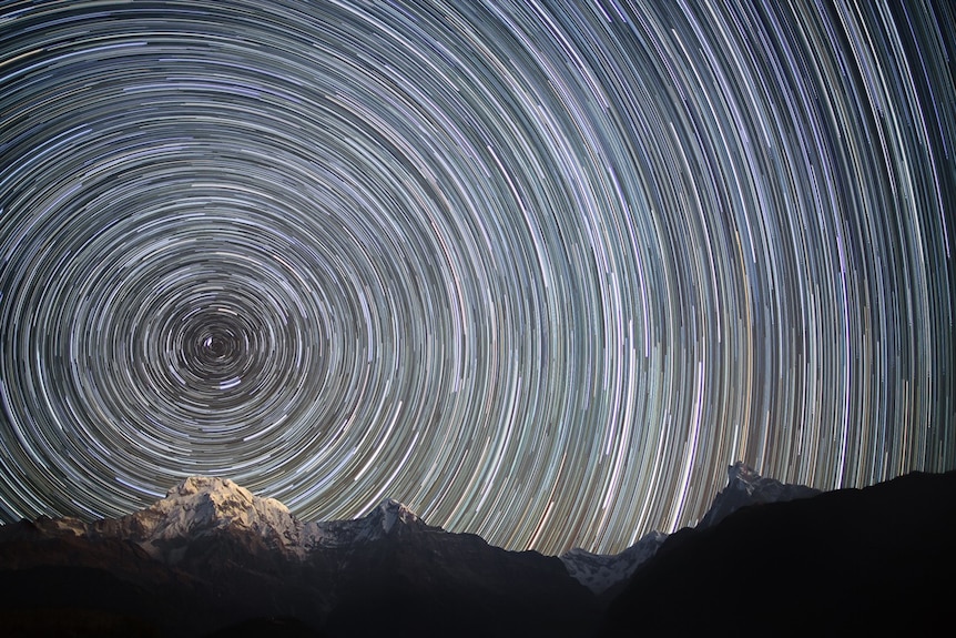 Stars traced out in circles above a snow-capped mountain range, showing the Earth's rotation.