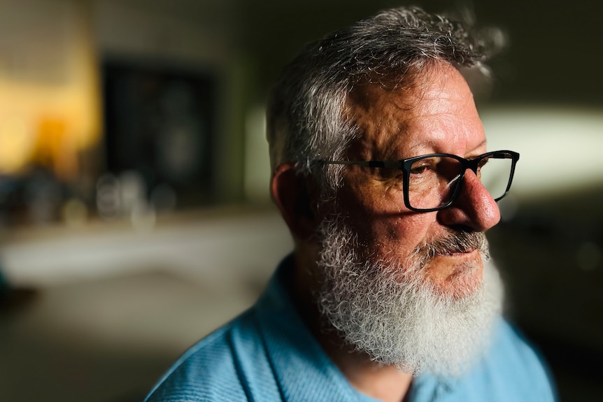 a man with a thick grey beard and hair, wearing black reading glasses