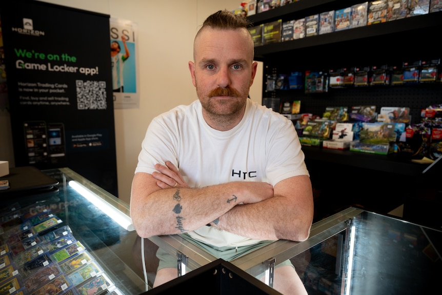 A man leans his arms over a glass counter in front of shelves displaying video games
