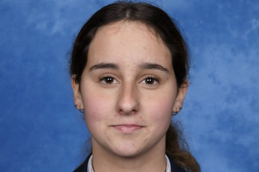 A teenage girl with long dark hair in a pony tail poses for her school photo in school uniform.