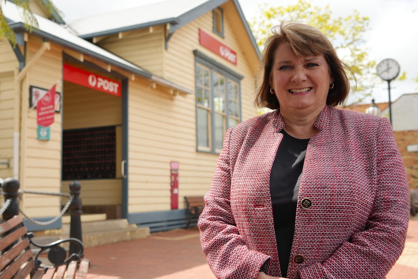 A smiling woman with a short brown bob standing in front of a town post office.