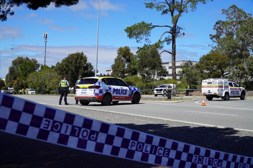 Police officers and vehicles parked on a road with police tape cordoning off a section. 