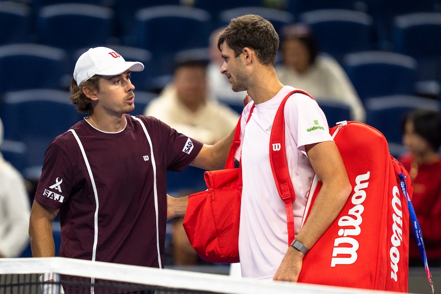 Australia's Alex de Minaur stands at the net and puts his hand on the shoulder of his opponent after a match.