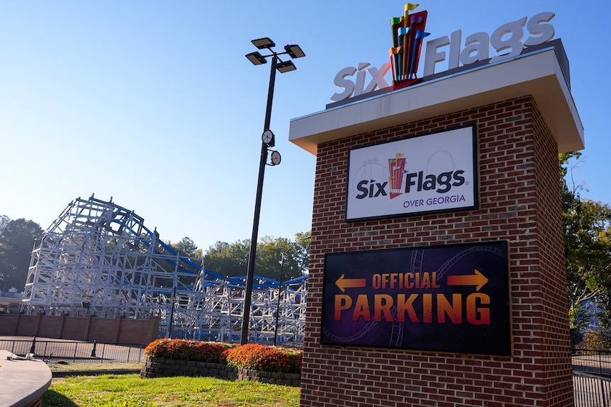 A brick sign with the name 'Six Flags over Georgia' and parking in front of a roller coaster.