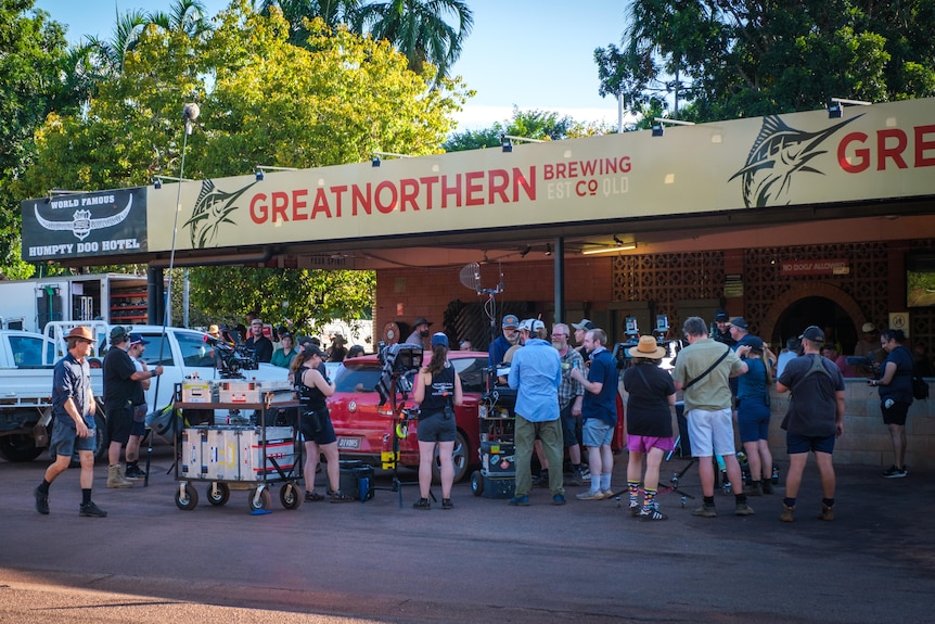 Men and women with film equipment outside a pub in a country area.
