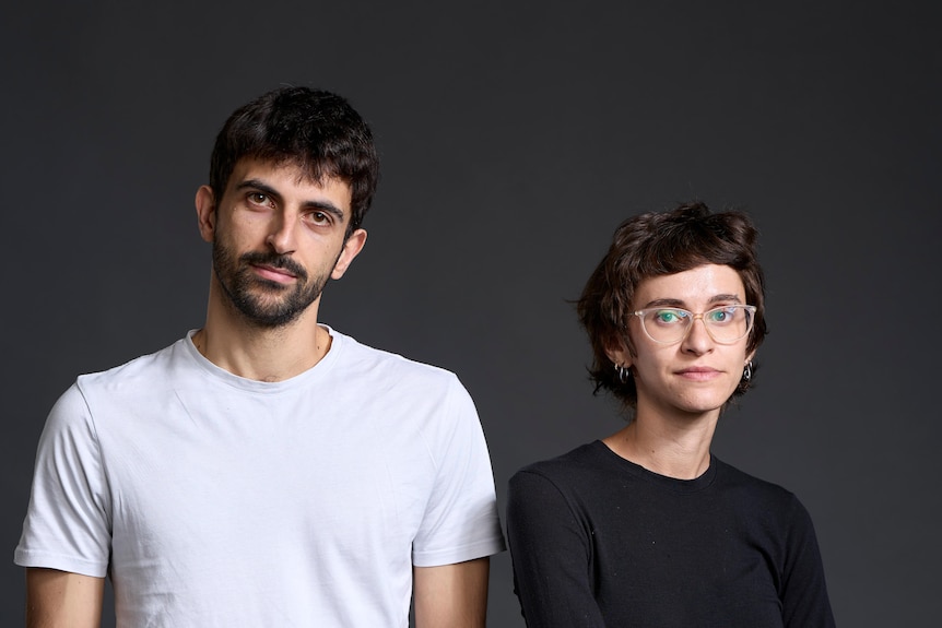 Two young people looking serious pose for a shot against a plain background