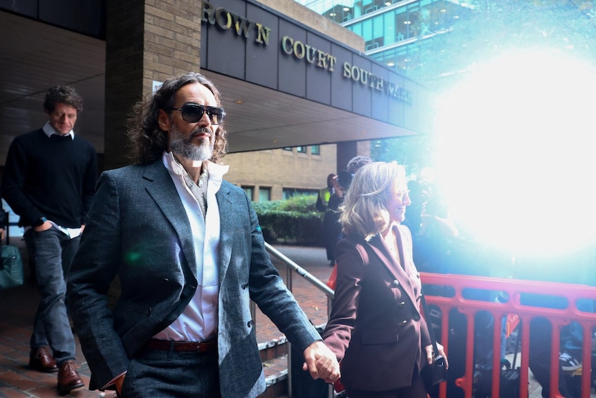 A man and a woman, both wearing suits and walking outside a building.