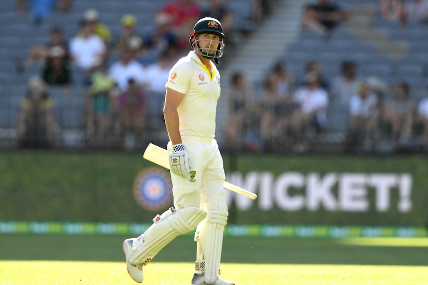 A man walks off a cricket field carrying a bat after being dismissed.