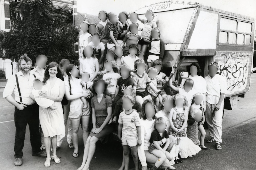 A black and white photo of a large group of children, with a few adults among the group, standing in front of a bus.