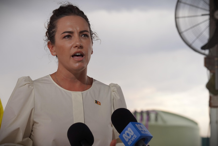 Chief Minister Lia Finocchiaro standing at microphones, white top, with outback background behind her.