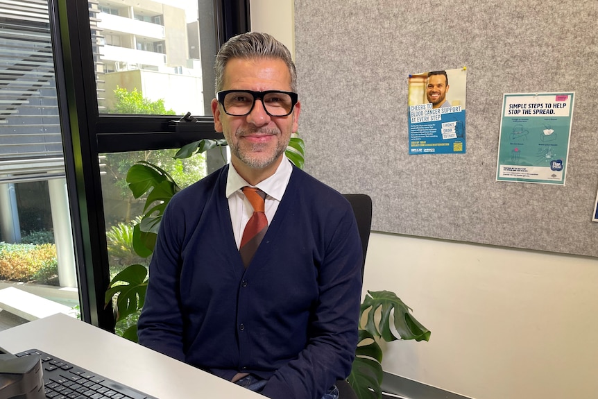 A man smiles from his desk.
