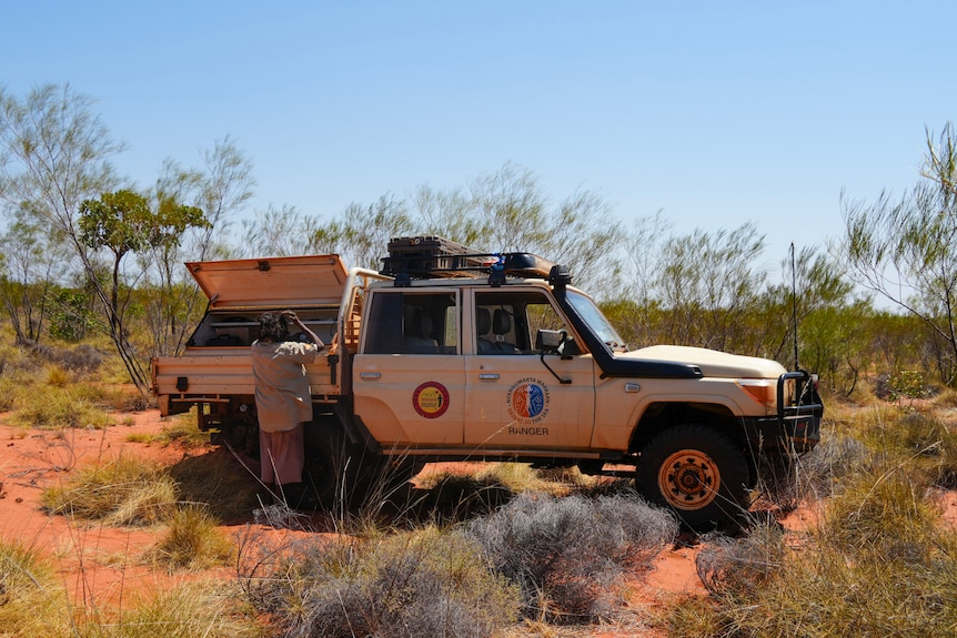 A four-wheel drive with a woman facing the trailer, opening the boot in shrub covered desert