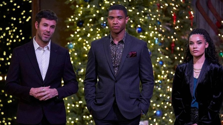Danny Escalante, Markelle Smith, Amanda Grace Jenkins stand in dark suits in front of Christmas trees lit up by lights.