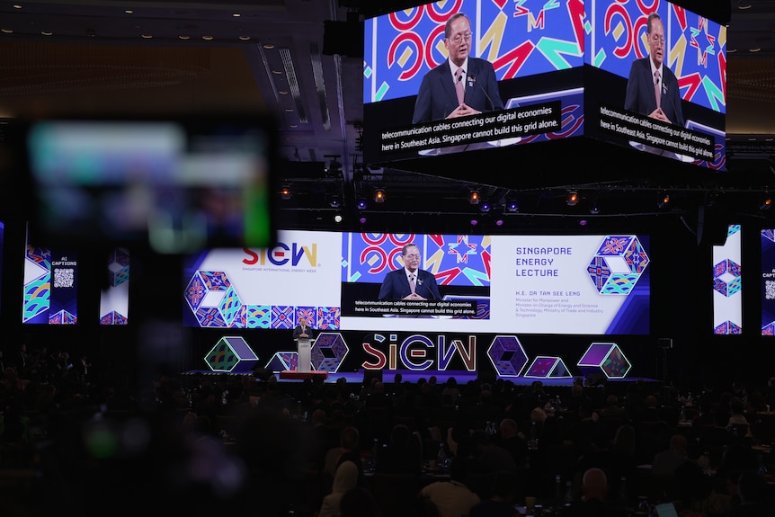 An array of large screens displaying a man talking from a podium. 