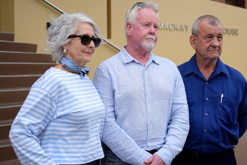 A woman and two men stand outside a building.